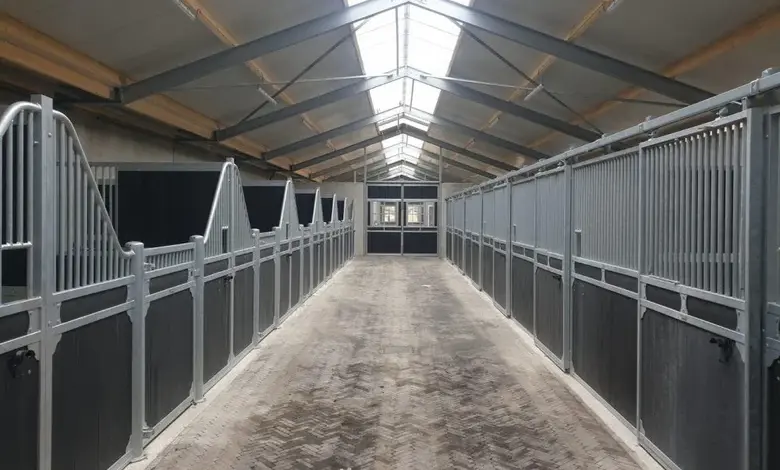 Moderní přístřešek pro koně s kovovými boxy a světlou střechou.