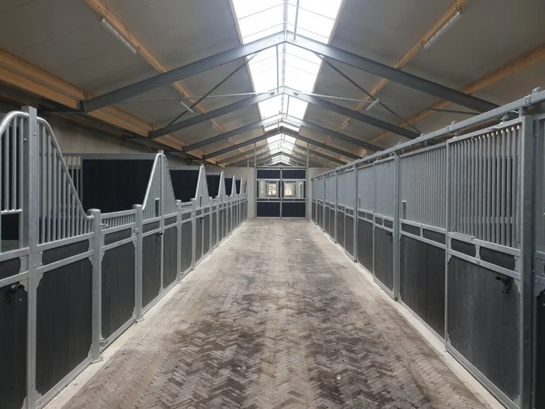 Moderní přístřešek pro koně s kovovými boxy a světlou střechou.