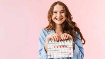 Dívka drží kalendář s červenými srdíčky na růžovém pozadí.