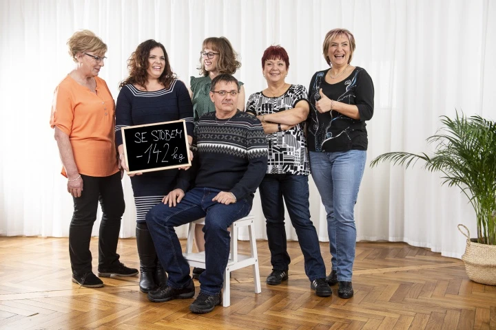 Skupina lidí s tabulkou o zhubnutí váhy.
