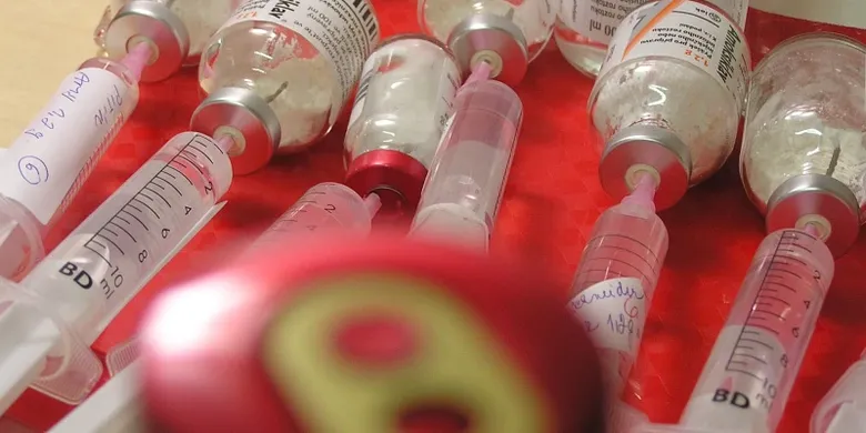 Skleněné lahvičky s antibiotiky připravené k podání injekcí na červeném povrchu.