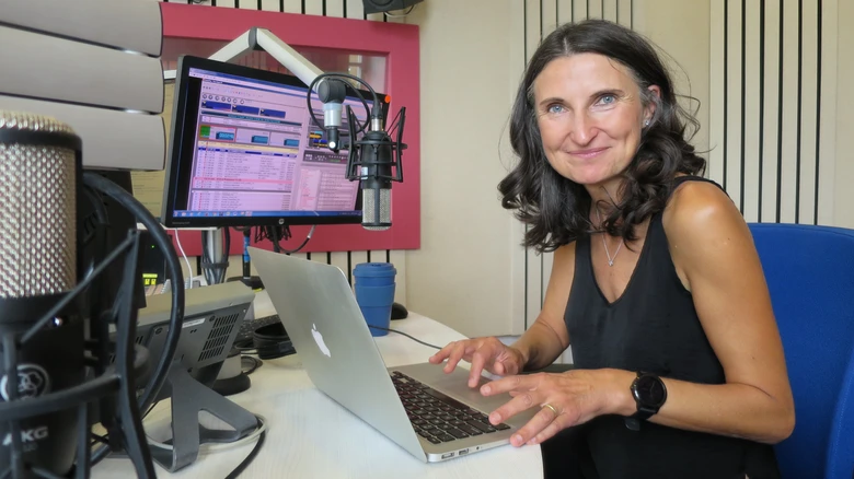 Žena pracuje na notebooku v rozhlasové studii s mikrofony.