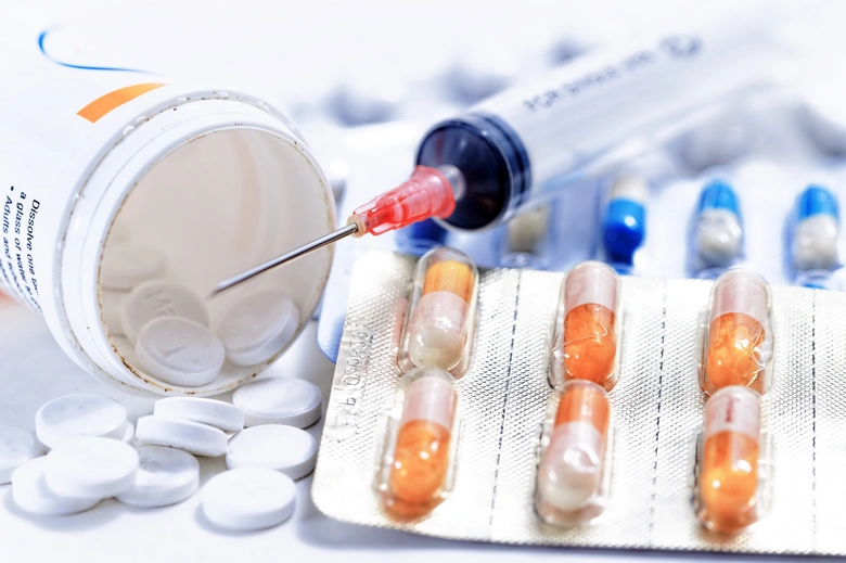 Bílé tablety, kapsle a jehla - obecná medicína bez steroidů.