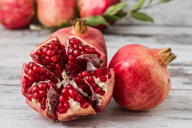 Řezané granátové jablko s červenými semínky na dřevěném povrchu.