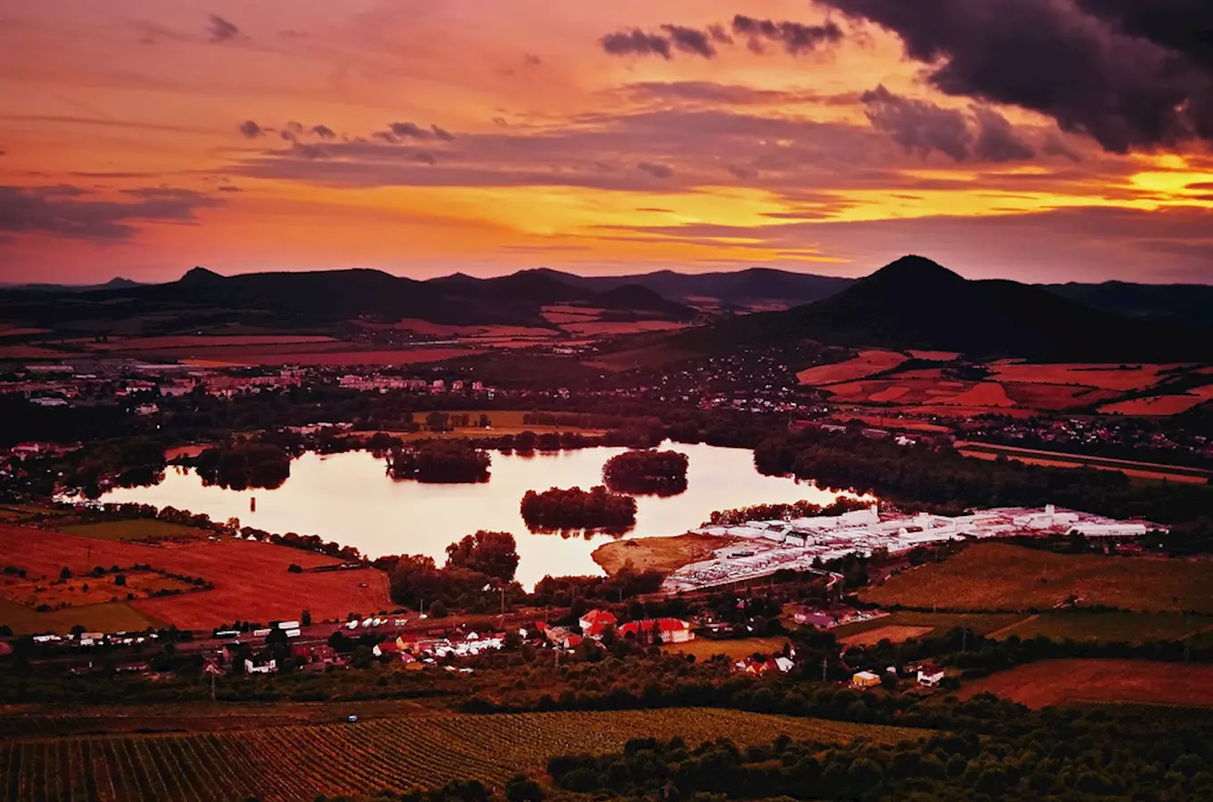 Západ slunce nad Žernoseckým jezerem s okolními poli a vesnicemi.