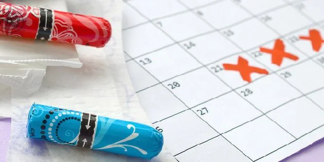 Dvě tampóny vedle kalendáře s označenými dny menstruace.