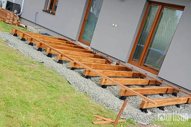 Dřevěné trámy pro terasu na kamínkách u domu.