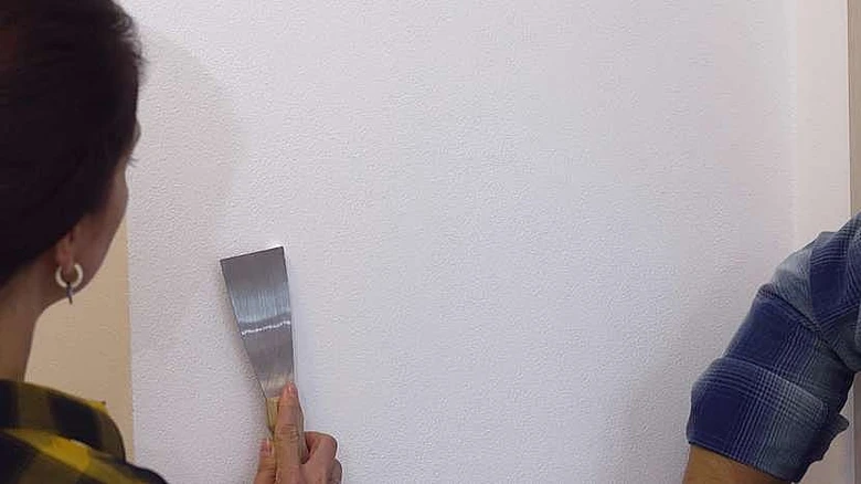 Osoba opravuje díru ve zdi pomocí špachtle.