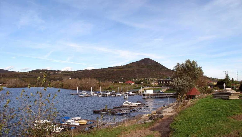Pohled na Žernosecké jezero s lodmi u mola a kopcem v pozadí.