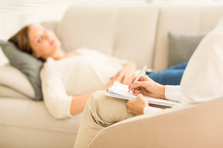 Žena leží na gauči během hypnoterapeutické sezení s terapeutem.