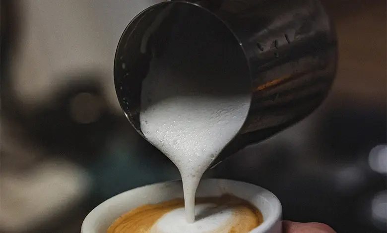 Barista nalévá horké mléko do šálku s kávou.