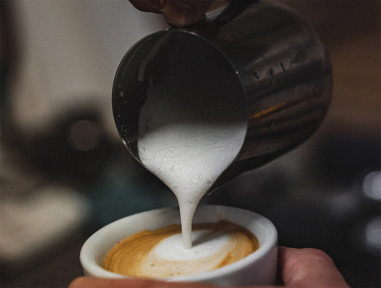 Barista nalévá horké mléko do šálku s kávou.