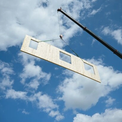 Velký dřevěný CLT panel je zvedán žebřicem na staveništi.