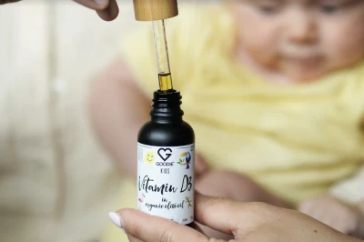 Ruce drží lahvičku vitaminu D před miminkem.